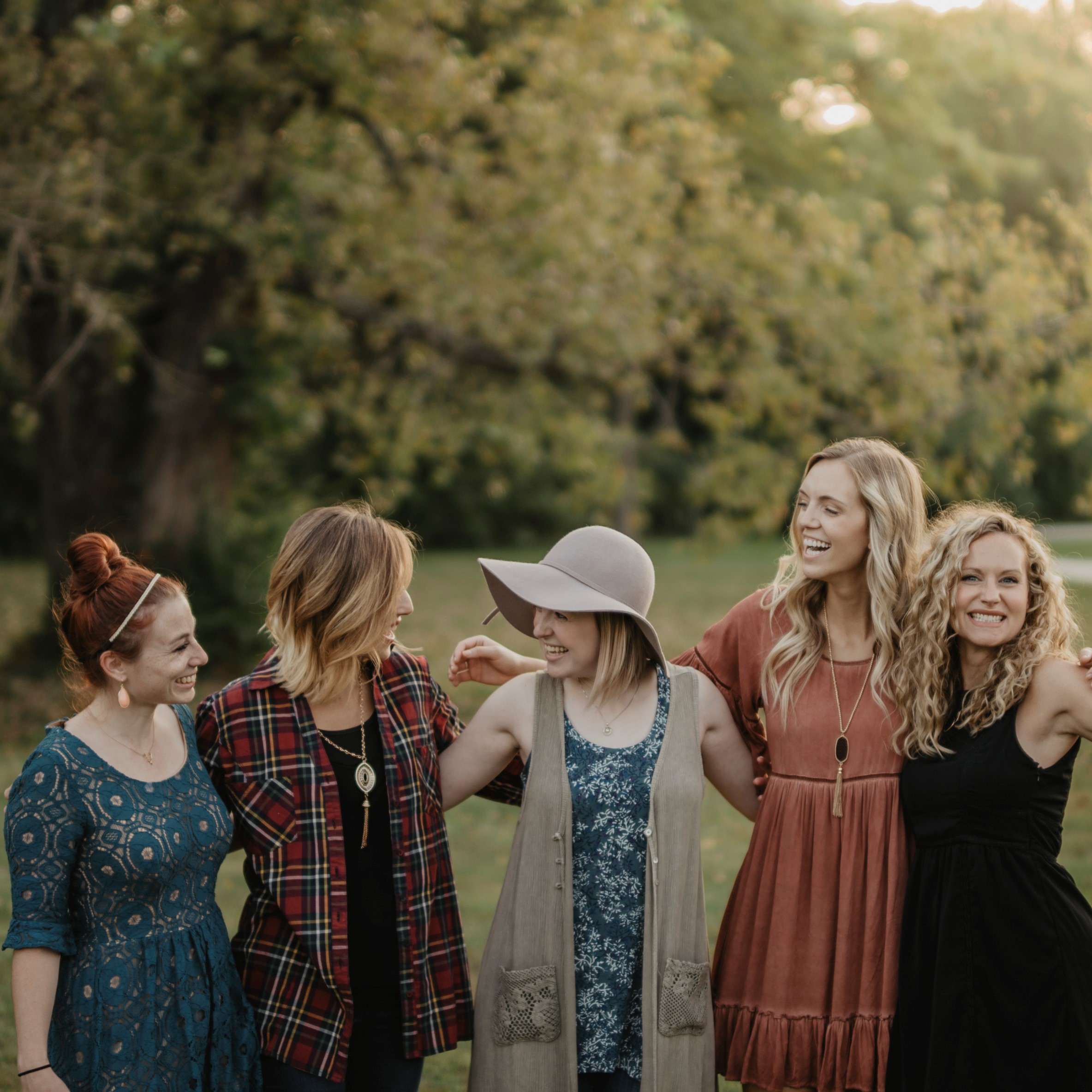 A group of young women in fall clothing standing outside with their arms around each other