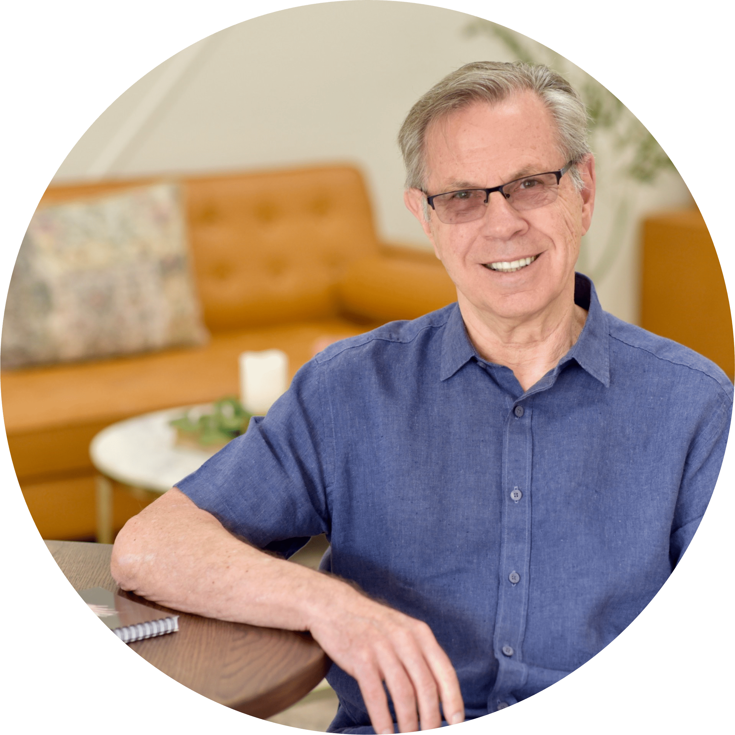 Smiling older man with glasses and olive polo shirt leaning crossed arms onto counter