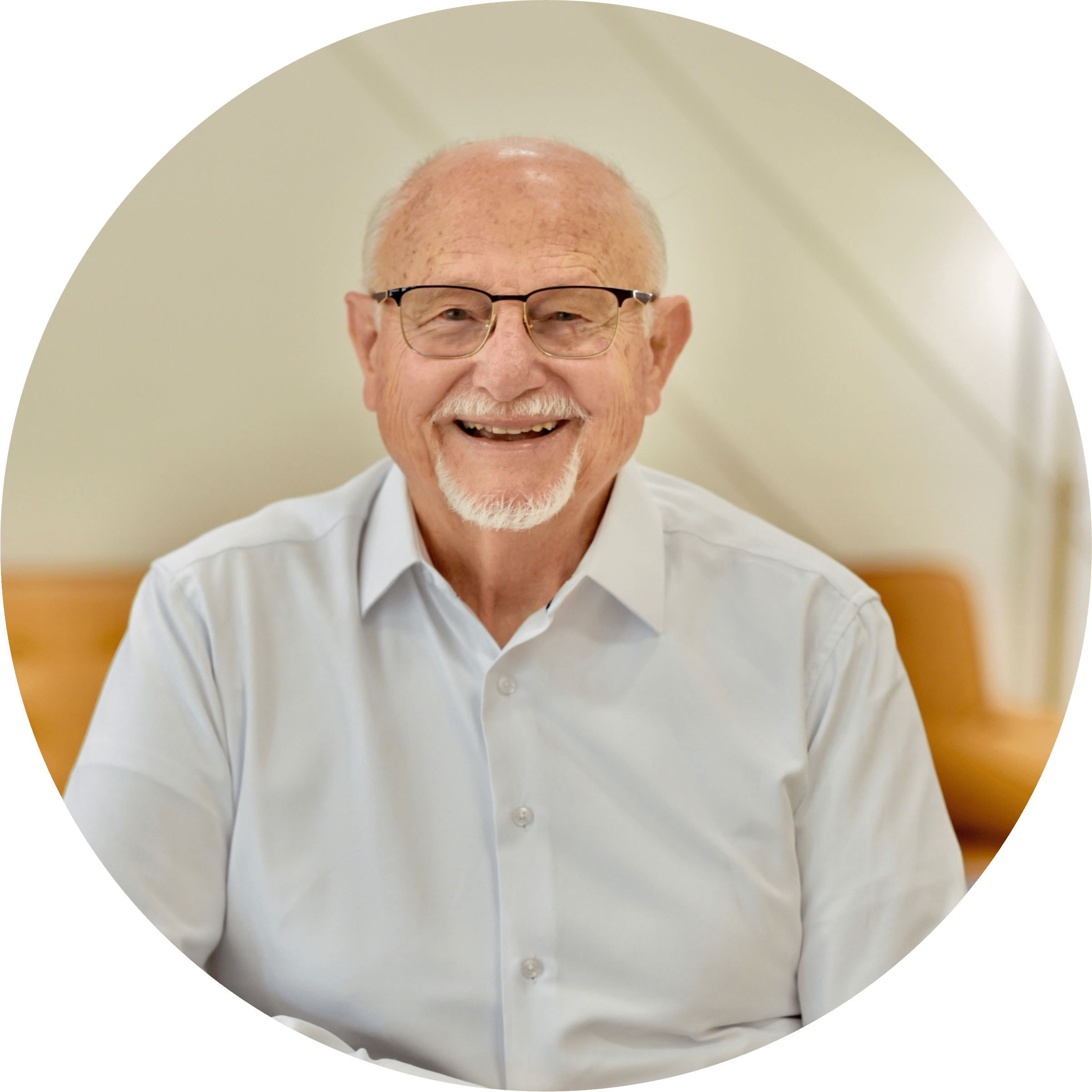 Friendly, smiling older man wearing glasses and blue short sleeved button front shirt placing hands on countertop