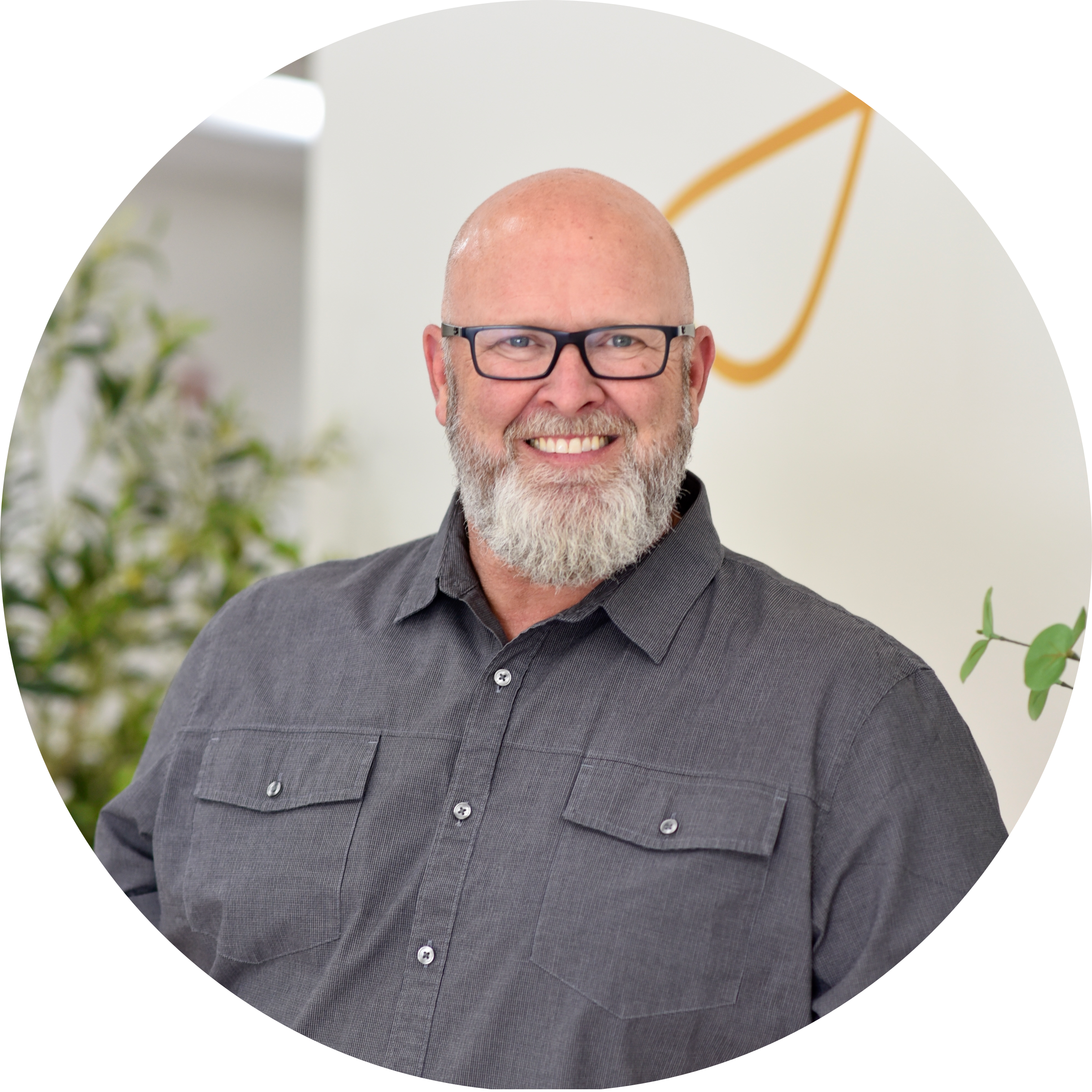 Friendly looking man with glasses, bald head and beard comfortably leaning forward on a leather sofa