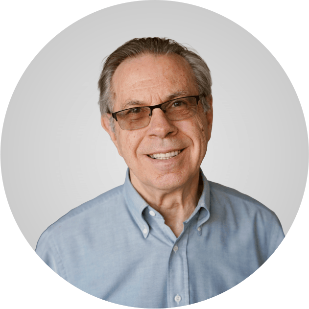 Smiling older man with glasses and olive polo shirt leaning crossed arms onto counter